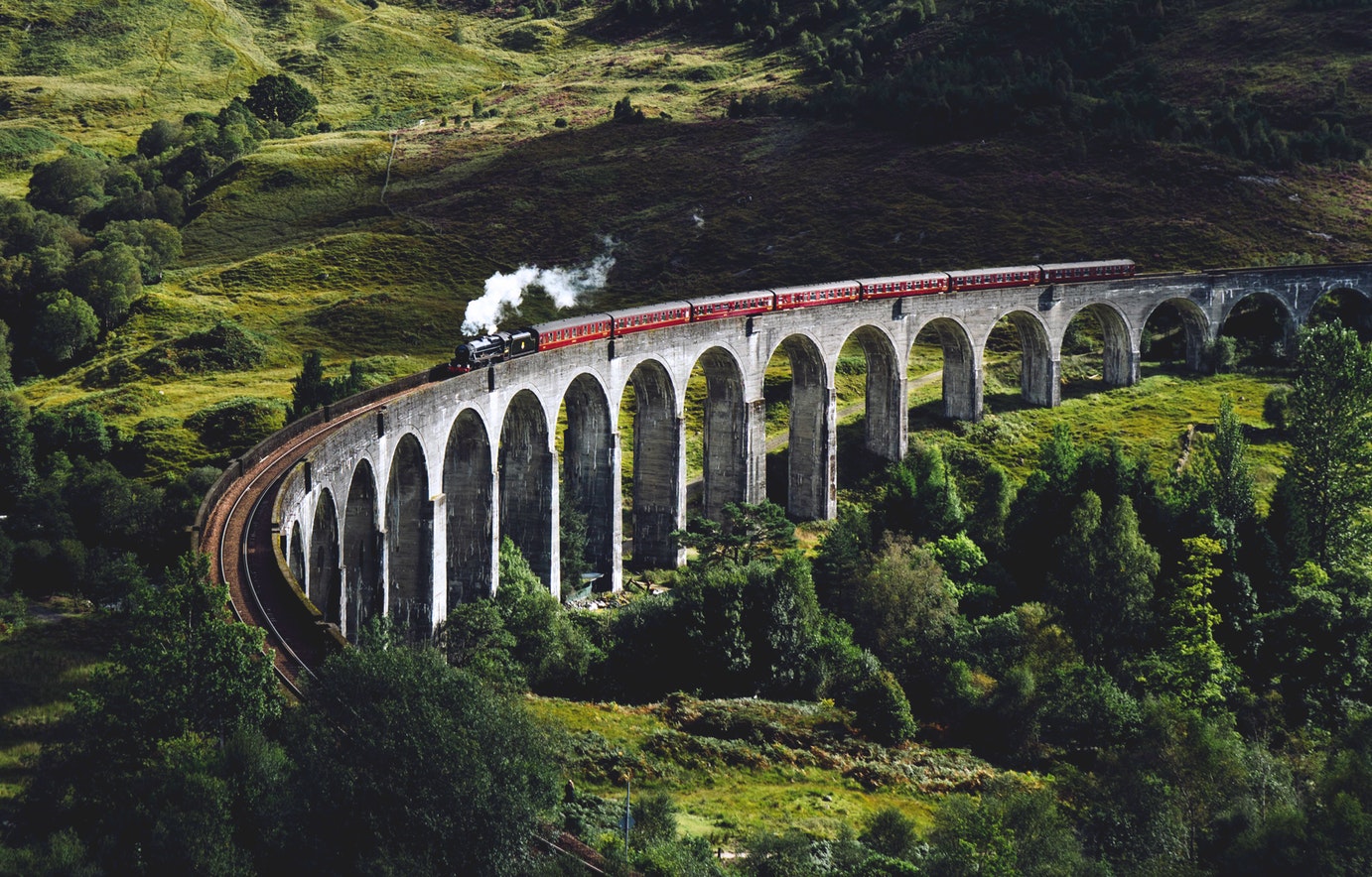 Un tren antiguo, con una locomotora de vapor, cruzando un puente de piedra con grandes arcos